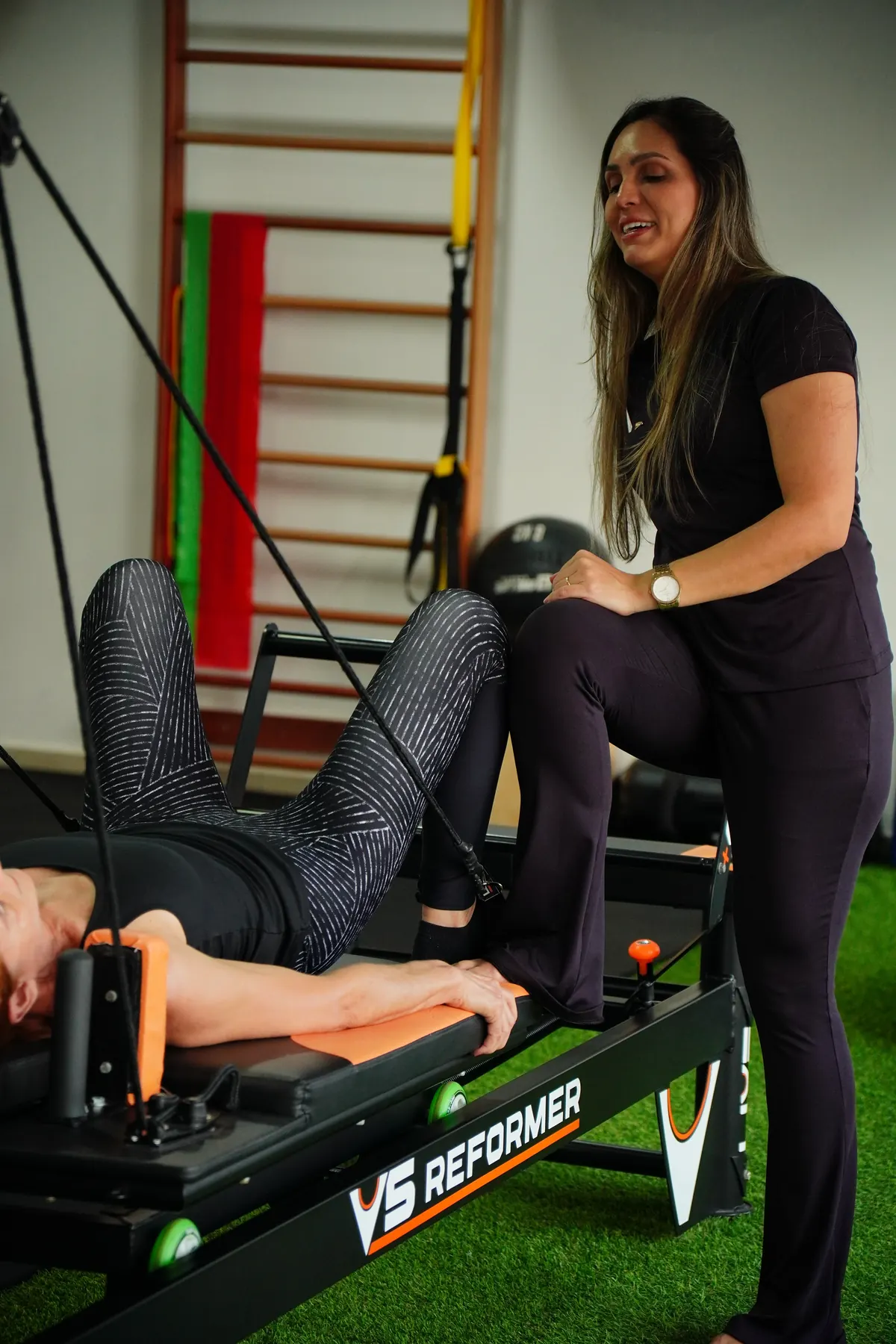 Fisioterapeuta acompanhando aluna durante exercício em aparelho Reformer na D’Life